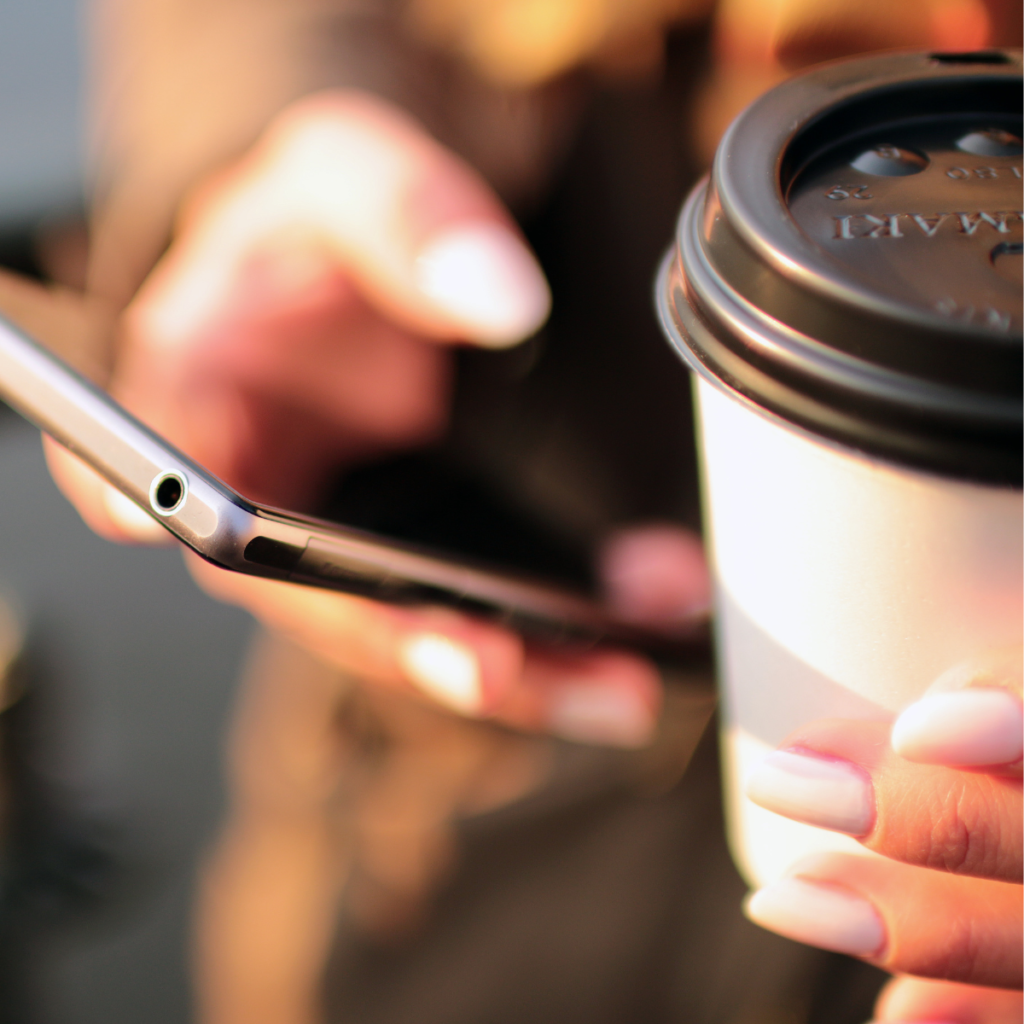 woman holding coffee in one hand and phone in the other